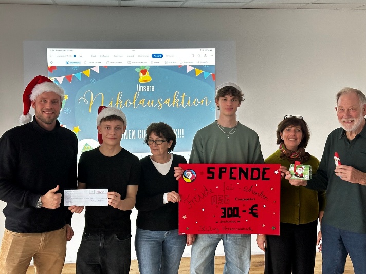 6 Personen stehen vor einem großen symbolischen Scheck und lächeln in die Kamera.